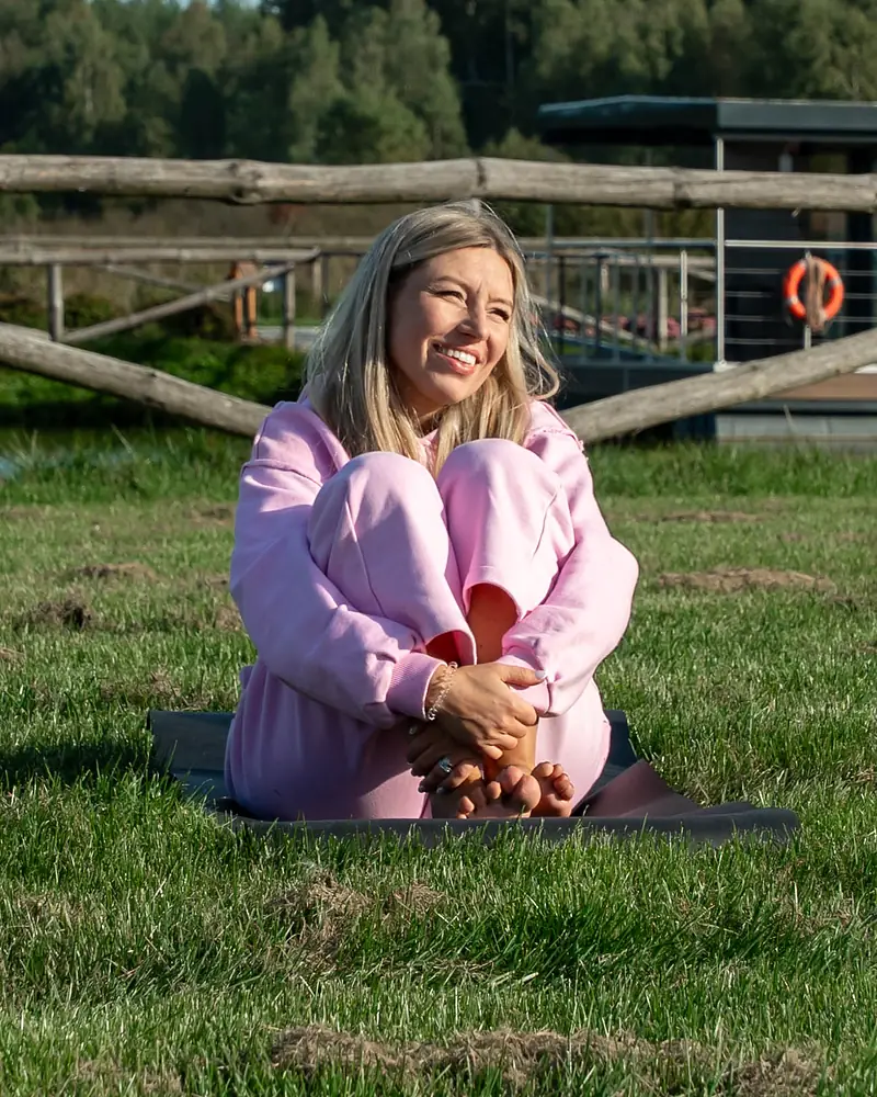 Ewa Wardęga sits on a mat on the grass and smiles at the sun